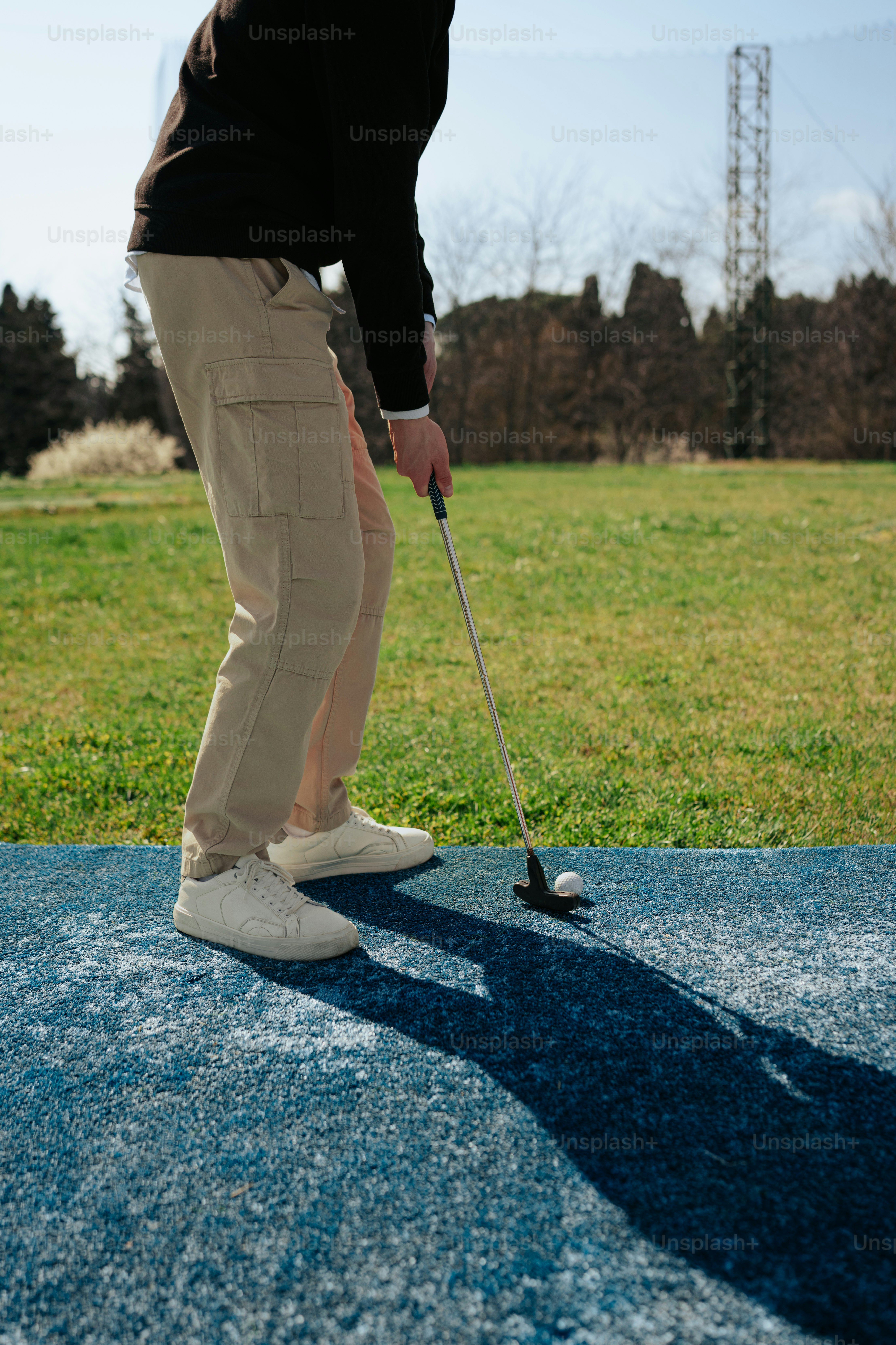 黒いシャツとカーキ色のズボンを着た男性がゴルフをしている