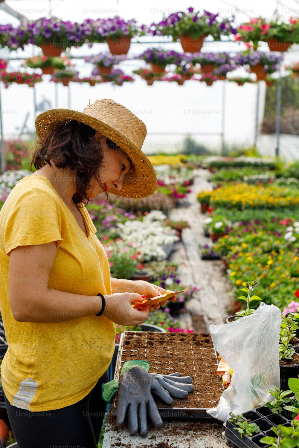 a woman in a yellow shirt and hat working in a greenhouse
