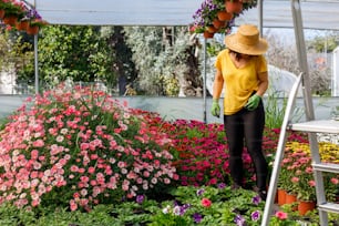 a woman in a yellow shirt and straw hat working in a garden