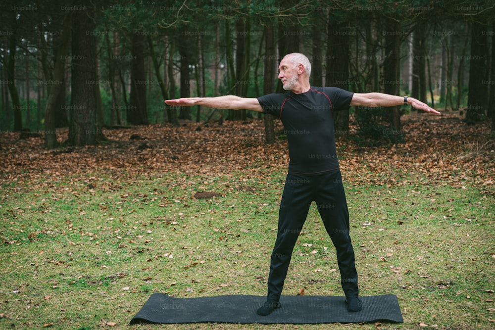 um homem de pé em um tapete de yoga no meio de uma floresta