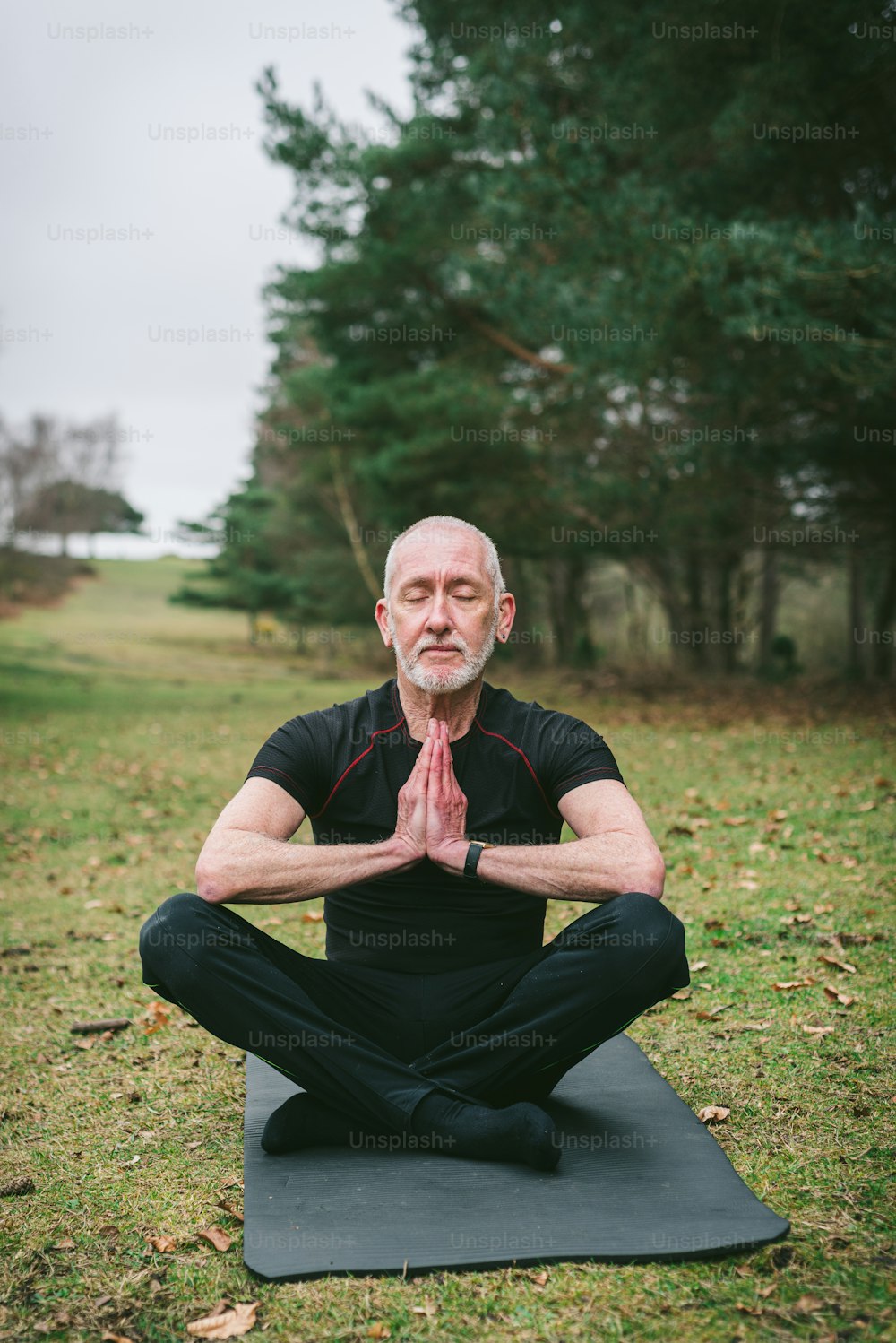 Un hombre sentado en una esterilla de yoga en un parque