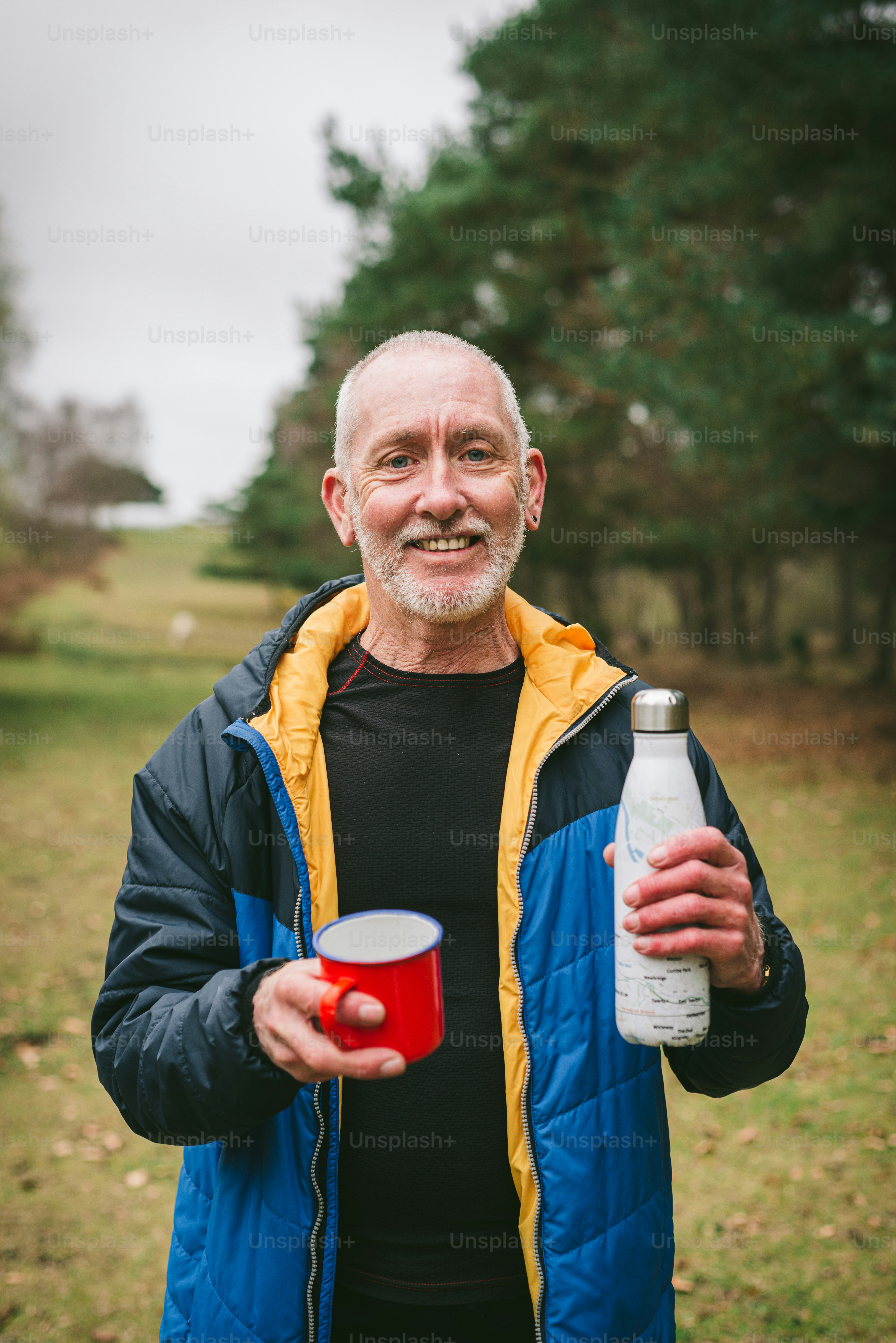 Ein Mann in einer blauen Jacke, der einen roten Becher und eine Flasche in der Hand hält
