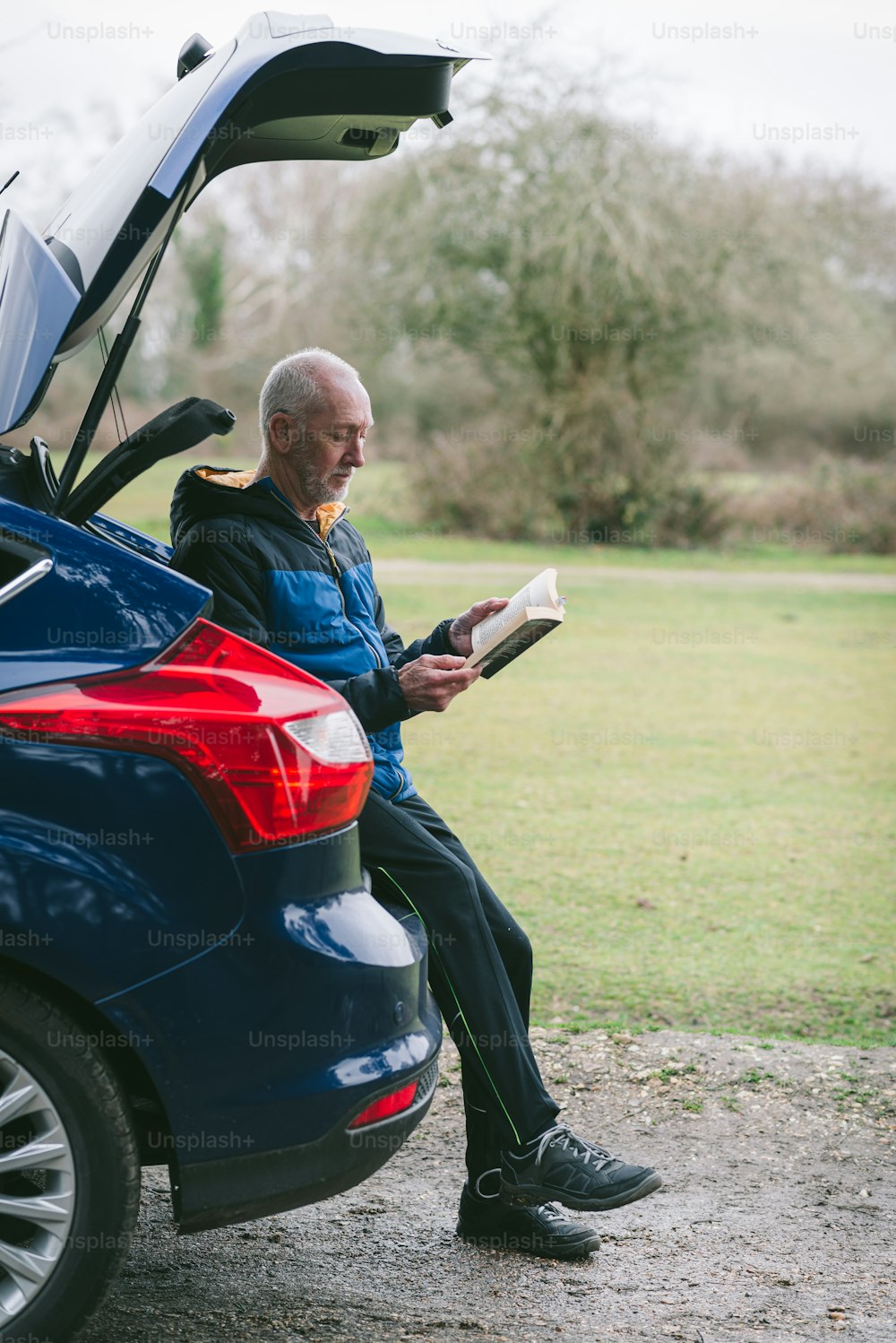 a man sitting on the trunk of a car reading a book