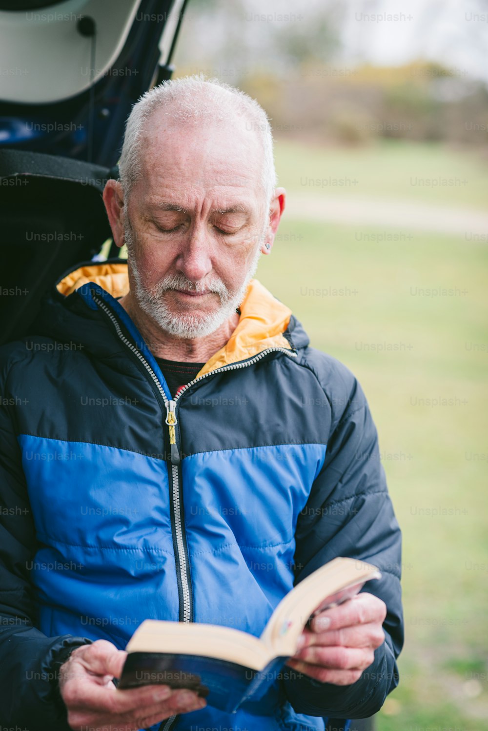 an older man is reading a book in the open trunk of a car