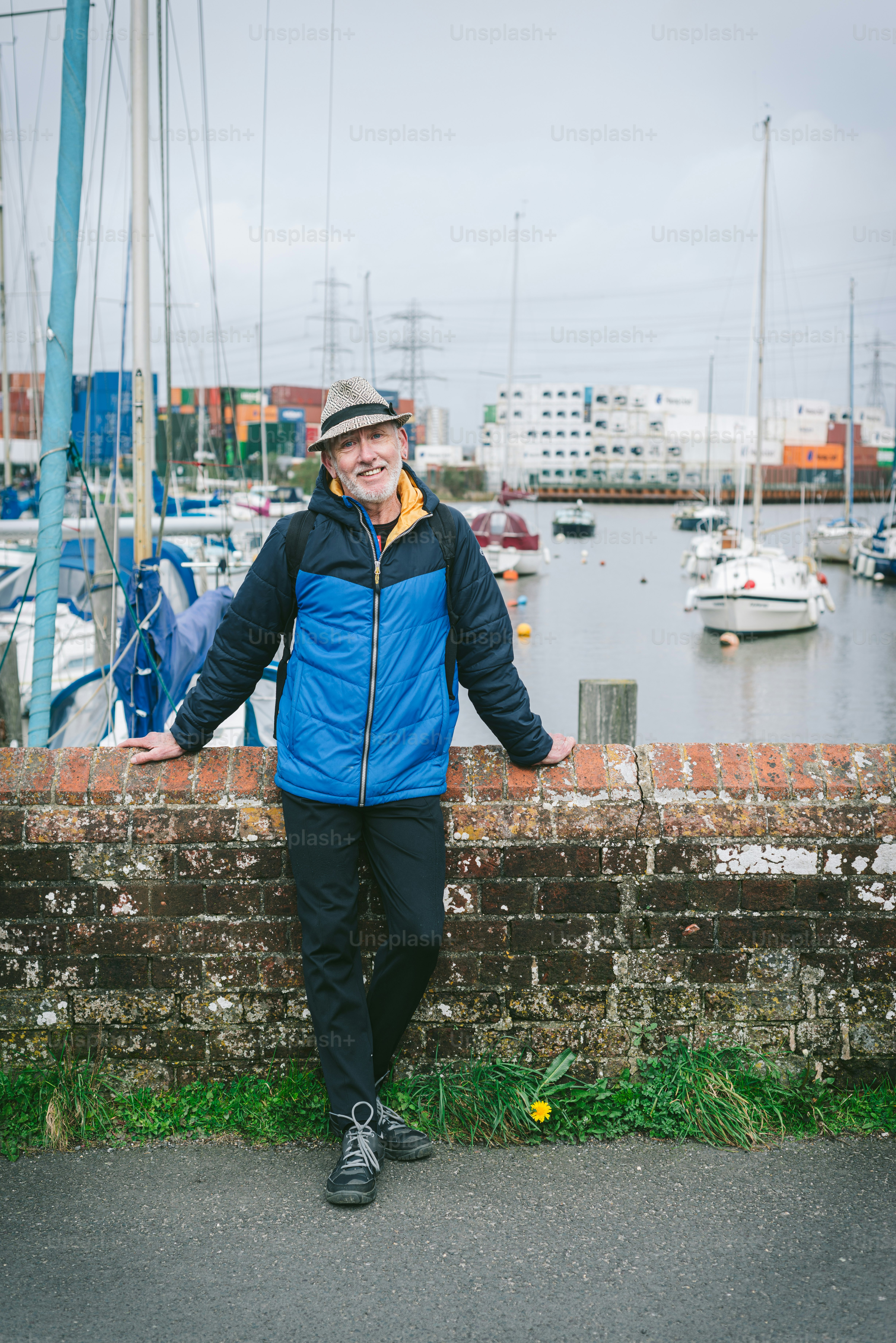 a man in a blue jacket leaning on a brick wall