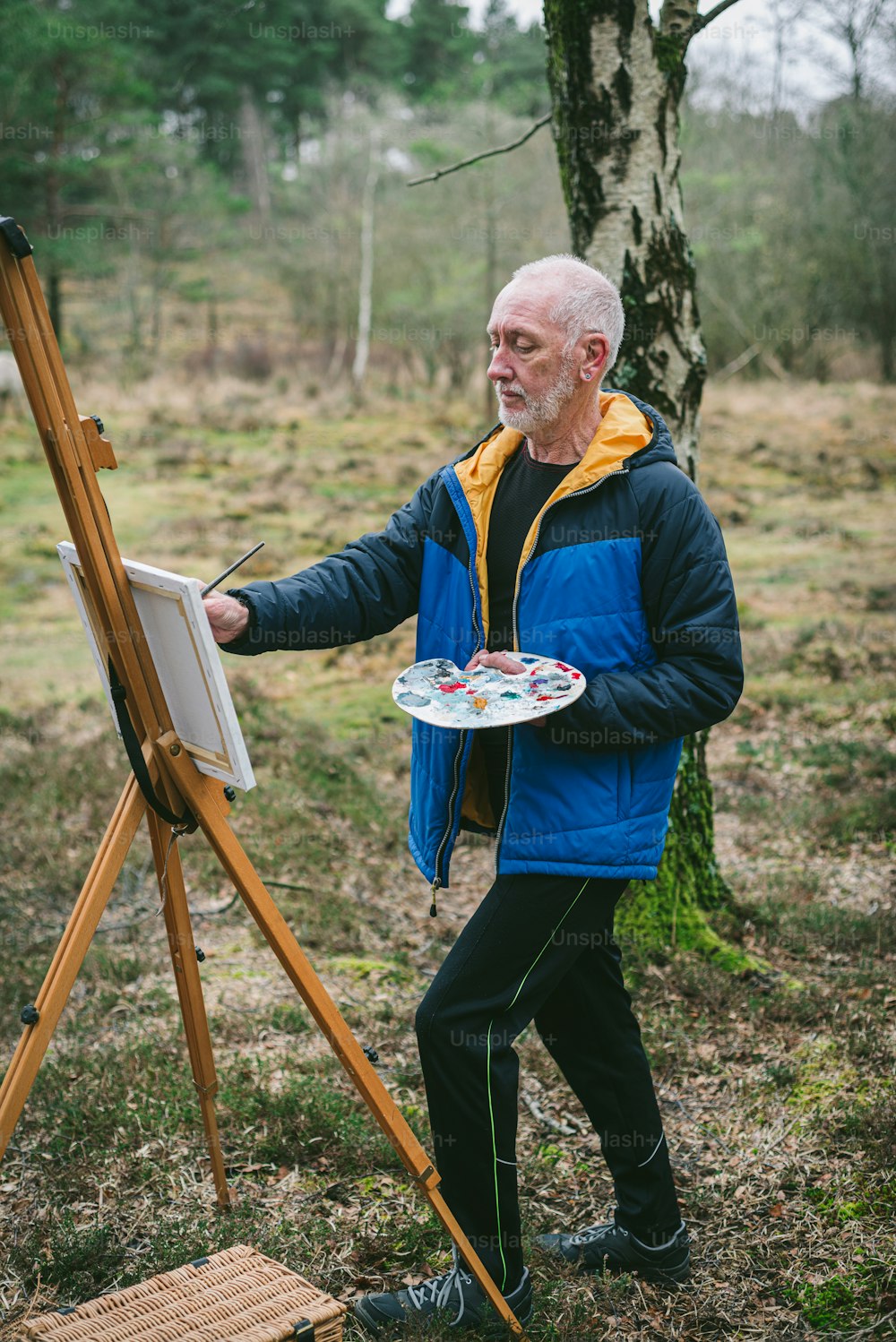 um homem de pé ao lado de um cavalete segurando uma pintura