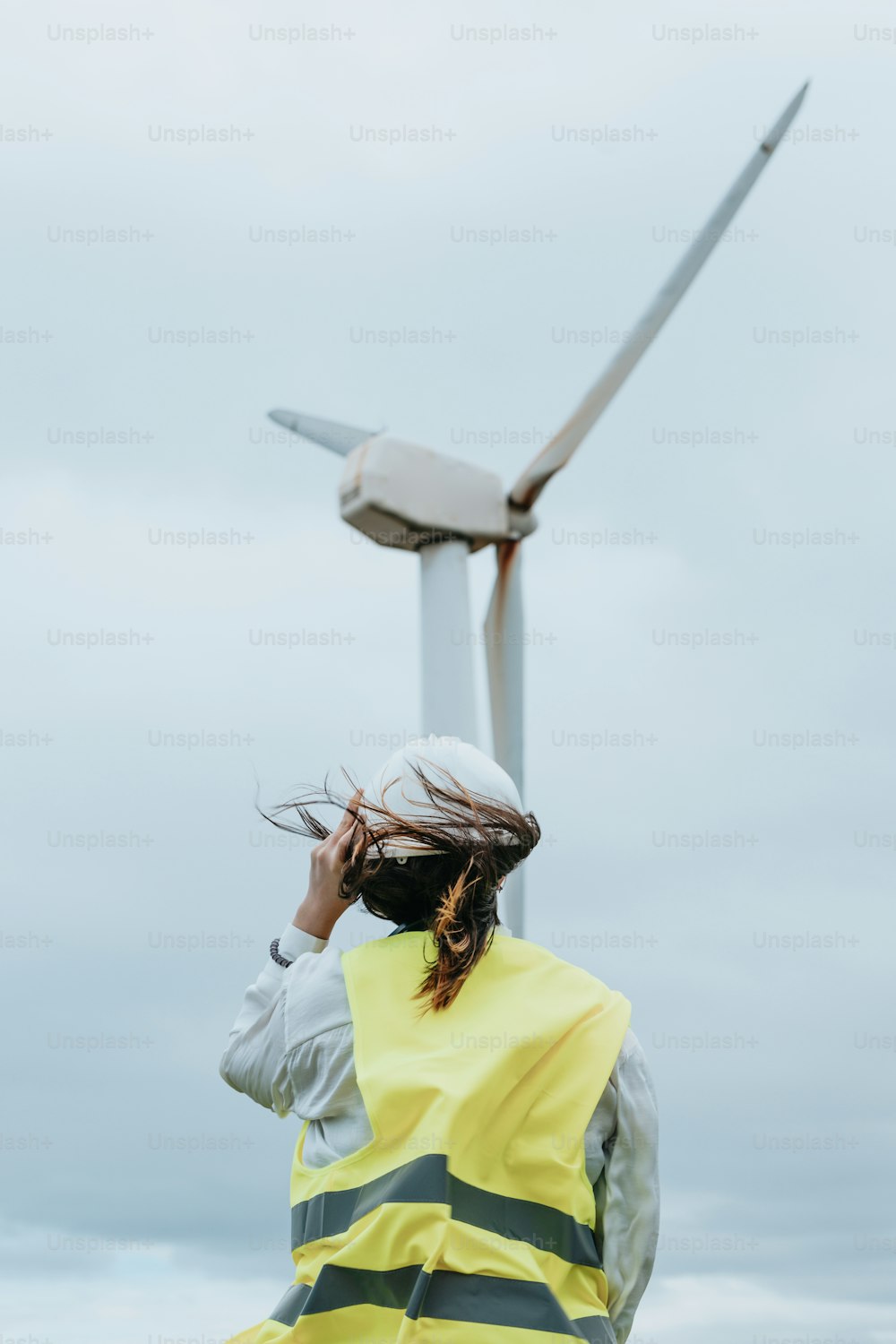 a woman in a yellow vest standing in front of a wind turbine