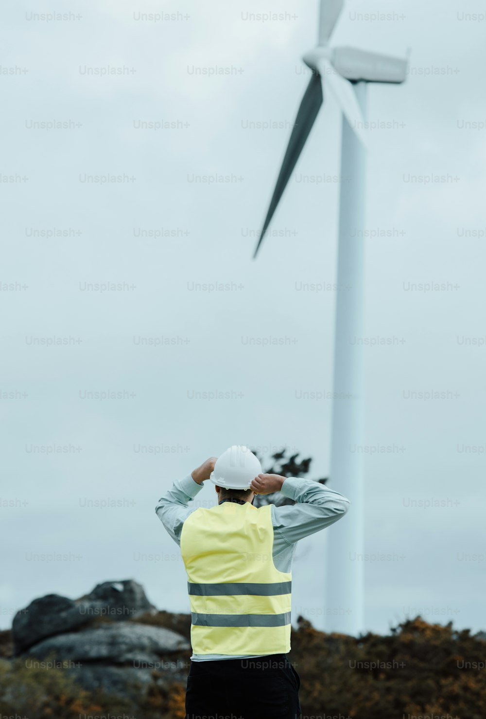 a man in a yellow vest standing in front of a wind turbine