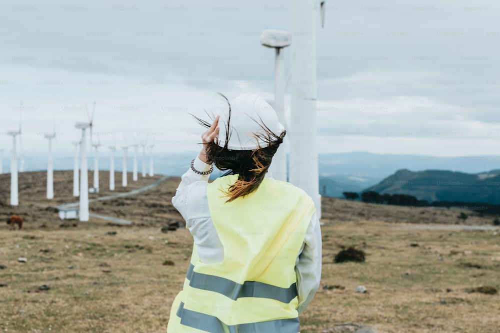 a woman in a yellow vest standing in front of a wind farm