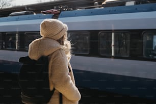 電車の前に立つバックパックを持つ女性
