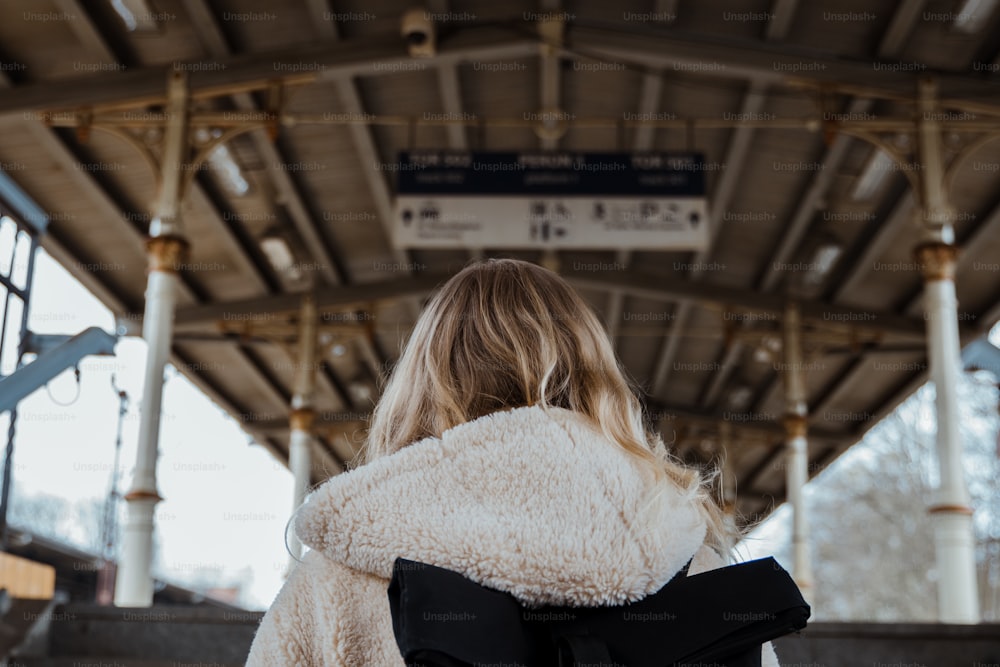 uma mulher em um casaco branco está esperando por um trem