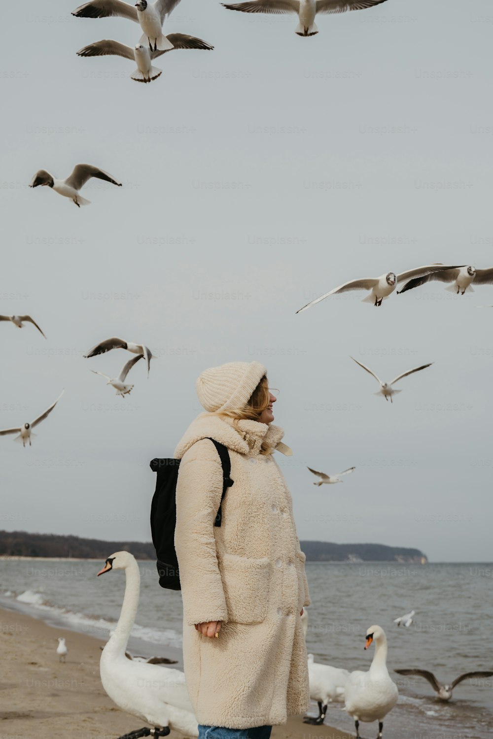 a woman standing on a beach next to a flock of birds