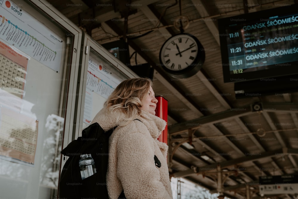 a woman standing in a train station next to a clock