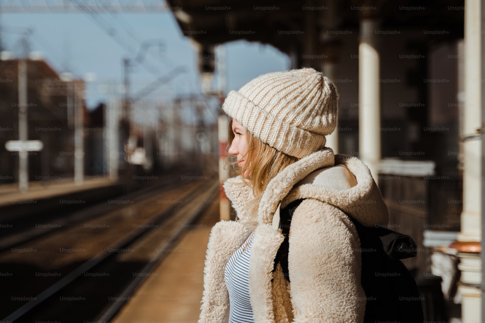 a woman in a hat and coat waiting for a train