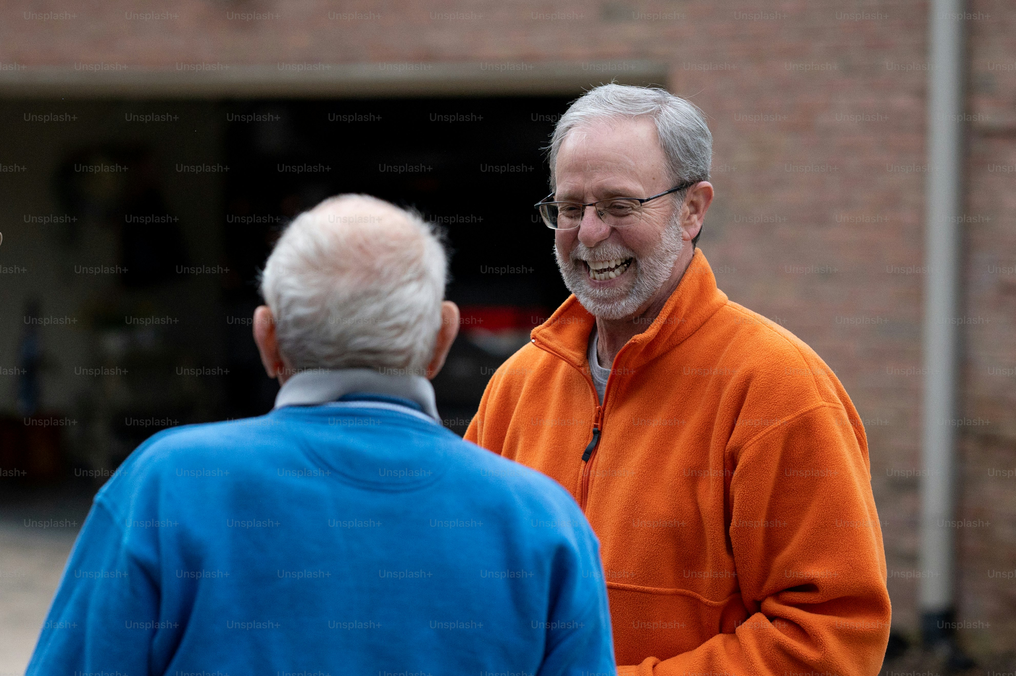 Un hombre con una chaqueta naranja hablando con un hombre con una chaqueta azul
