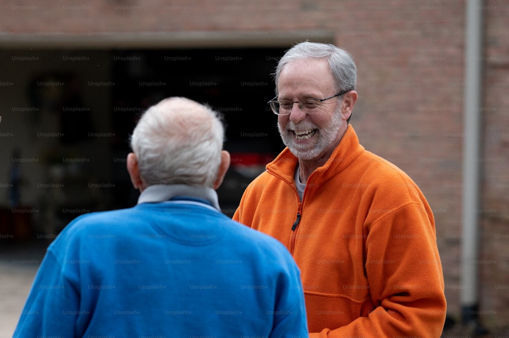 Un hombre con una chaqueta naranja hablando con un hombre con una chaqueta azul