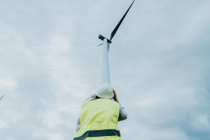 uma pessoa em uma jaqueta amarela de pé ao lado de uma turbina eólica