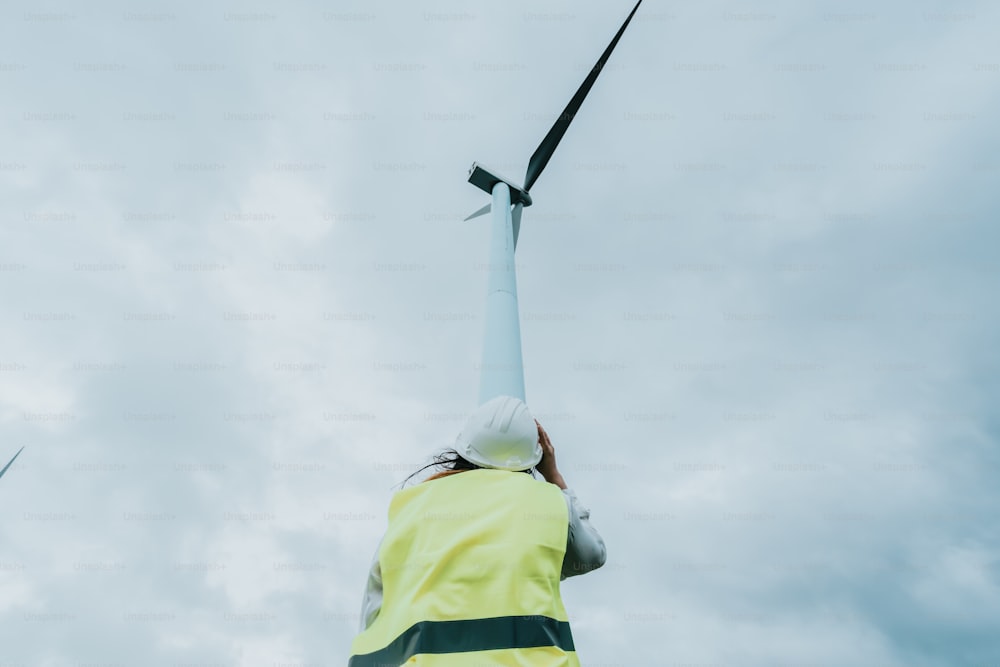 a person in a yellow jacket standing next to a wind turbine