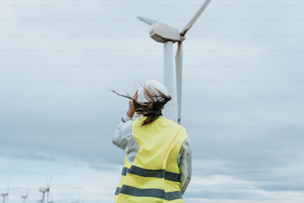 a woman in a yellow vest standing next to a wind turbine
