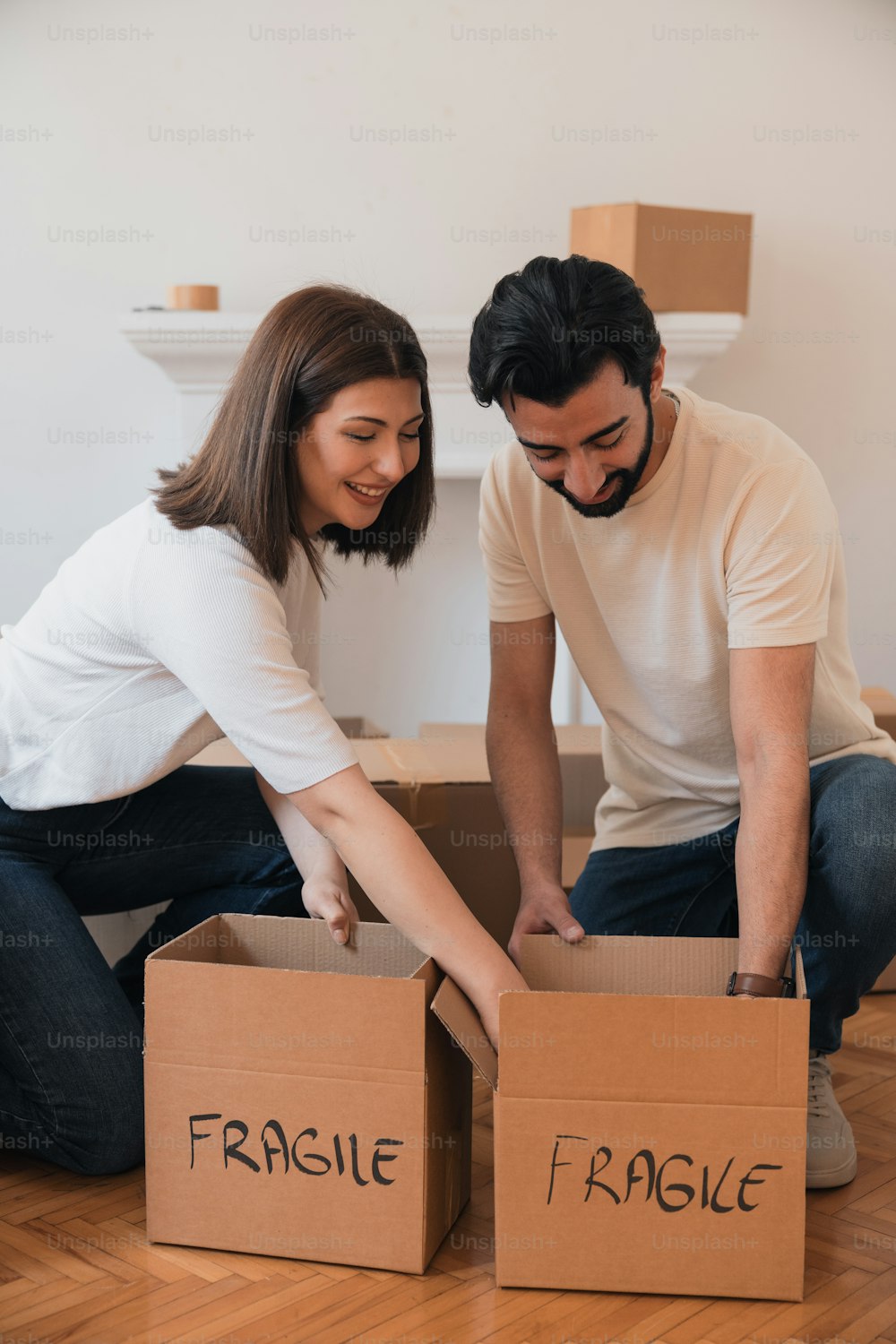 a man and a woman sitting on the floor opening a box