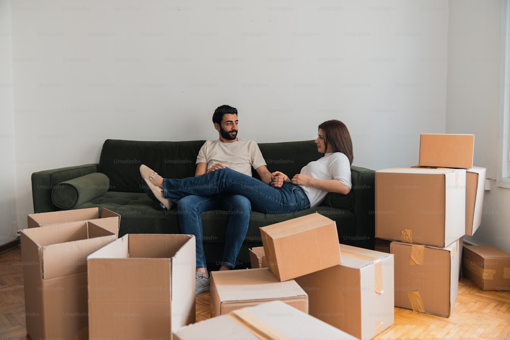 a man and woman sitting on a couch surrounded by boxes