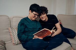 two people sitting on a couch reading a book