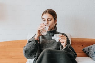 a woman sitting on a bed drinking a glass of water