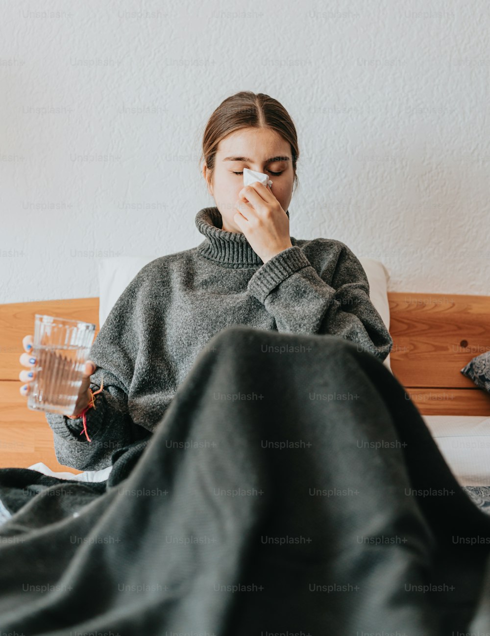 a woman sitting on a bed with a blanket covering her face