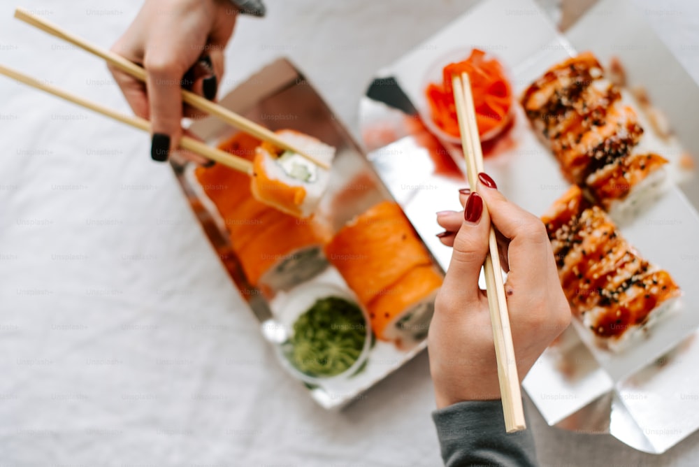 a person holding chopsticks over a plate of sushi