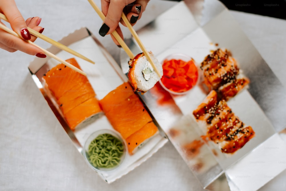 Una persona sosteniendo palillos sobre una caja de sushi