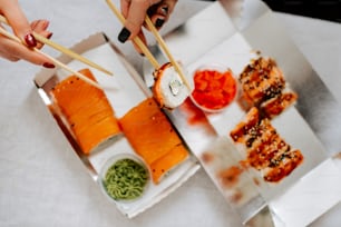 a person holding chopsticks over a box of sushi