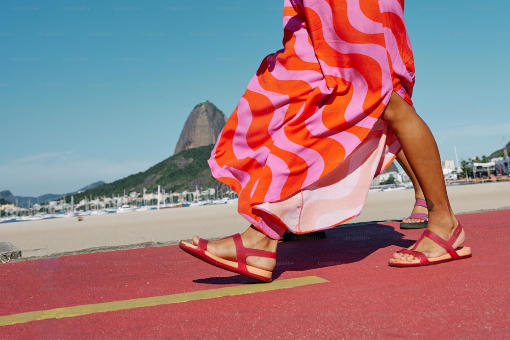 uma mulher em um vestido rosa e laranja andando em uma praia