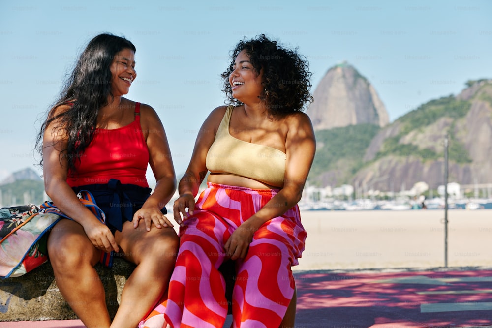 two women sitting next to each other on a beach