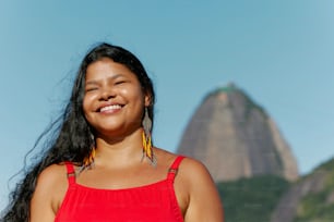 a woman in a red top smiles in front of a mountain