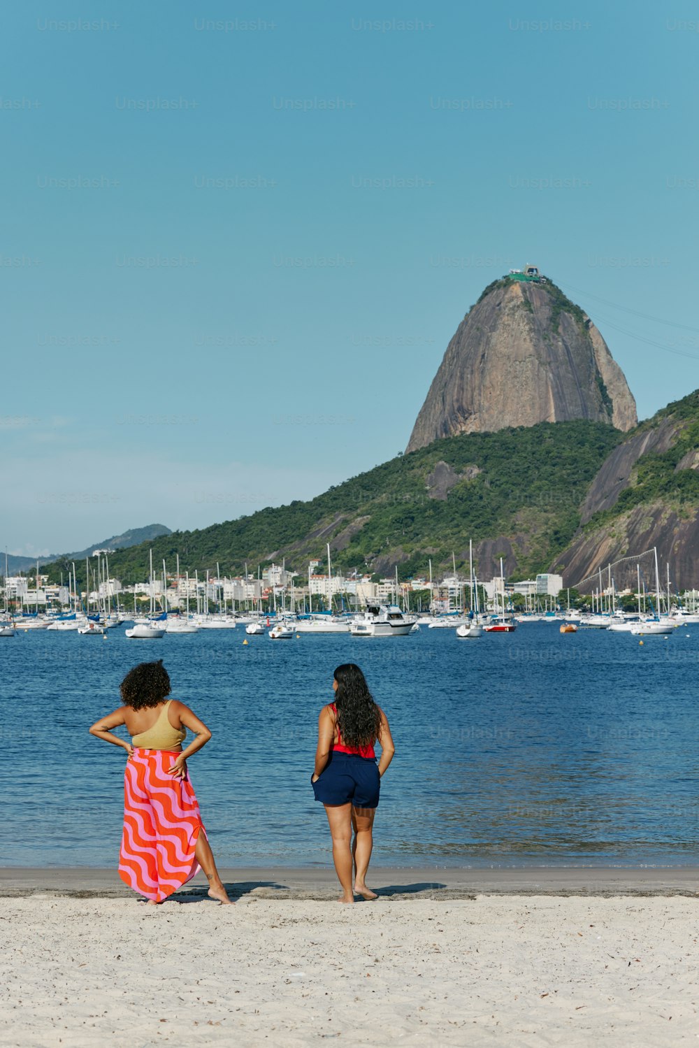 a couple of women standing on top of a sandy beach