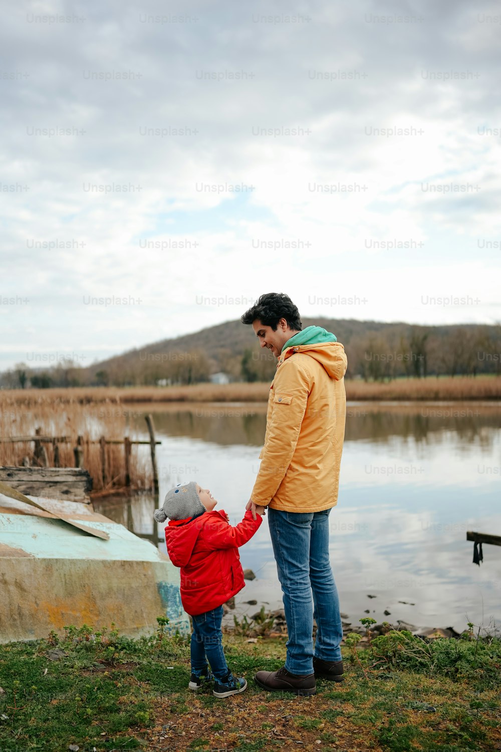 Un hombre sosteniendo la mano de un niño pequeño cerca de un cuerpo de agua