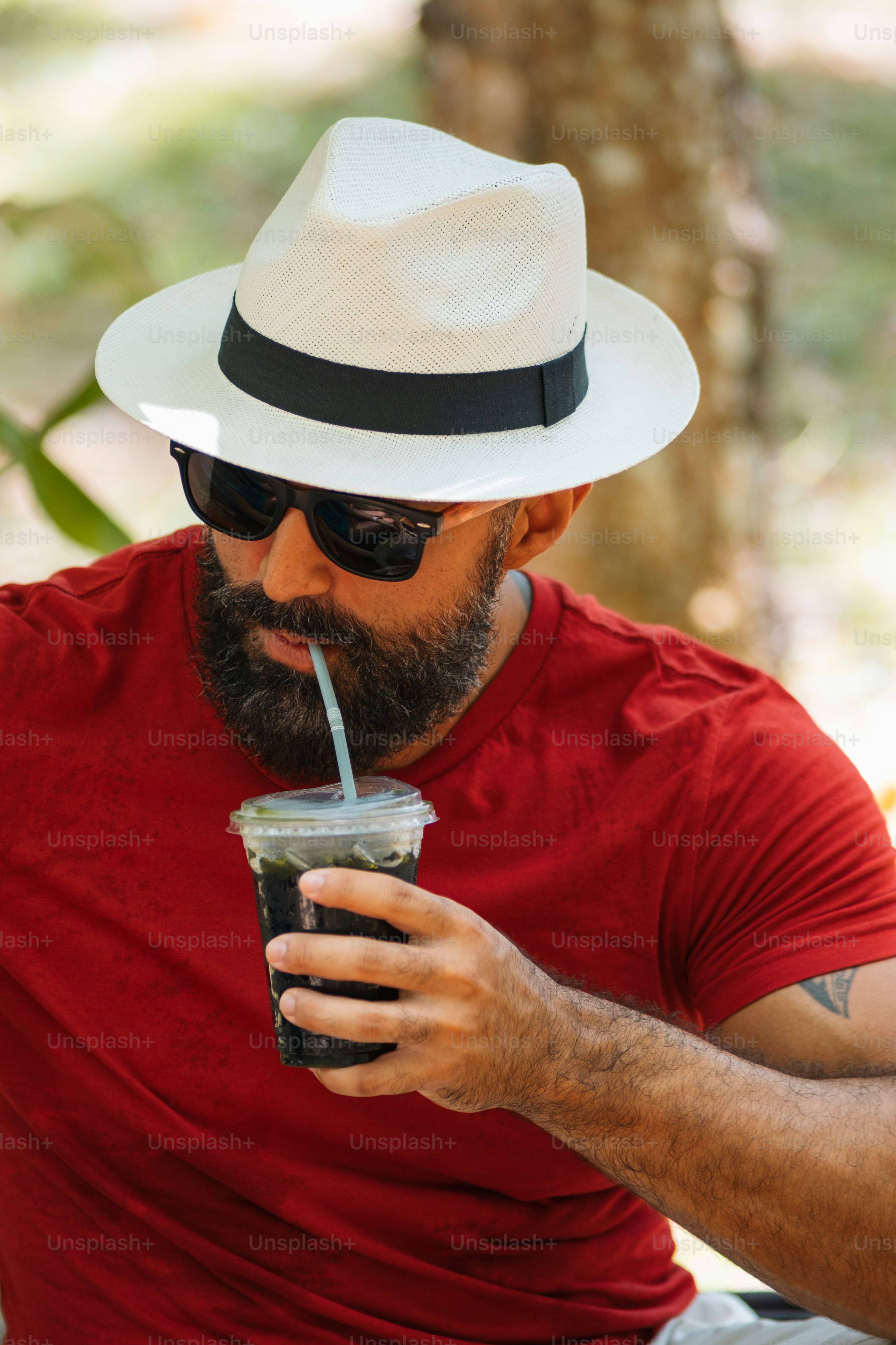 Un hombre con sombrero y gafas de sol bebiendo una bebida