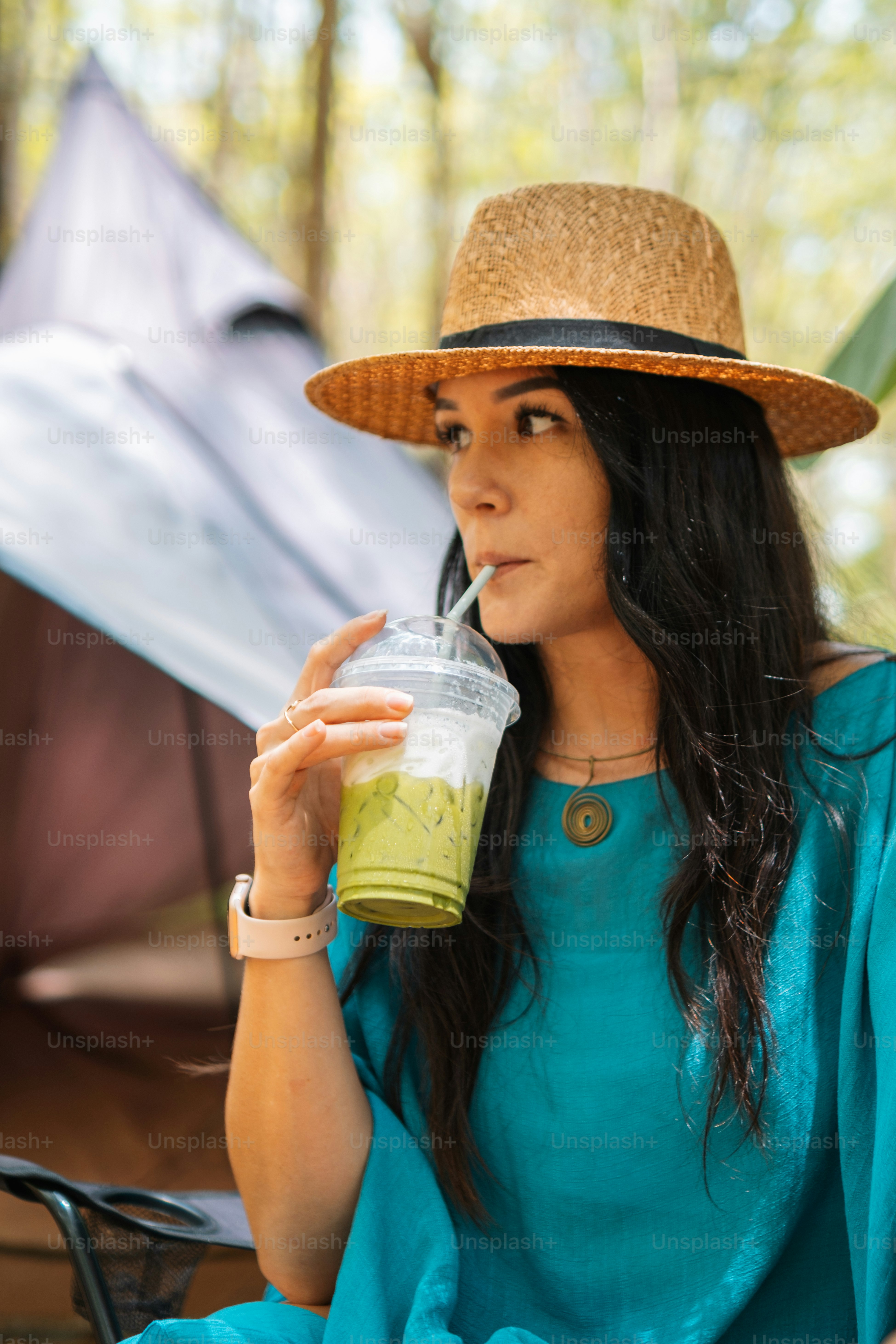 Una mujer con un sombrero de paja bebiendo un batido verde