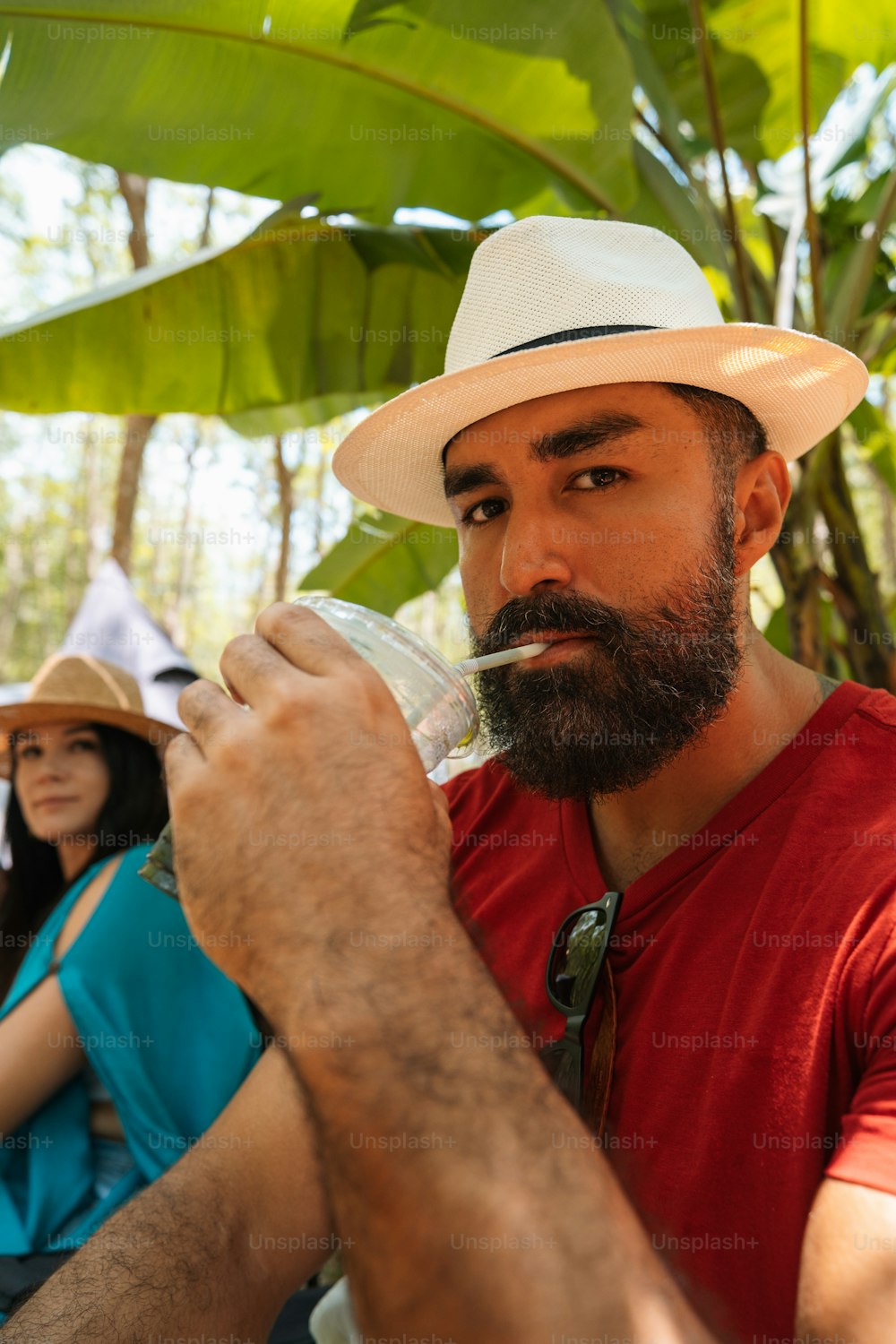 a man with a beard and a straw hat drinking from a water bottle