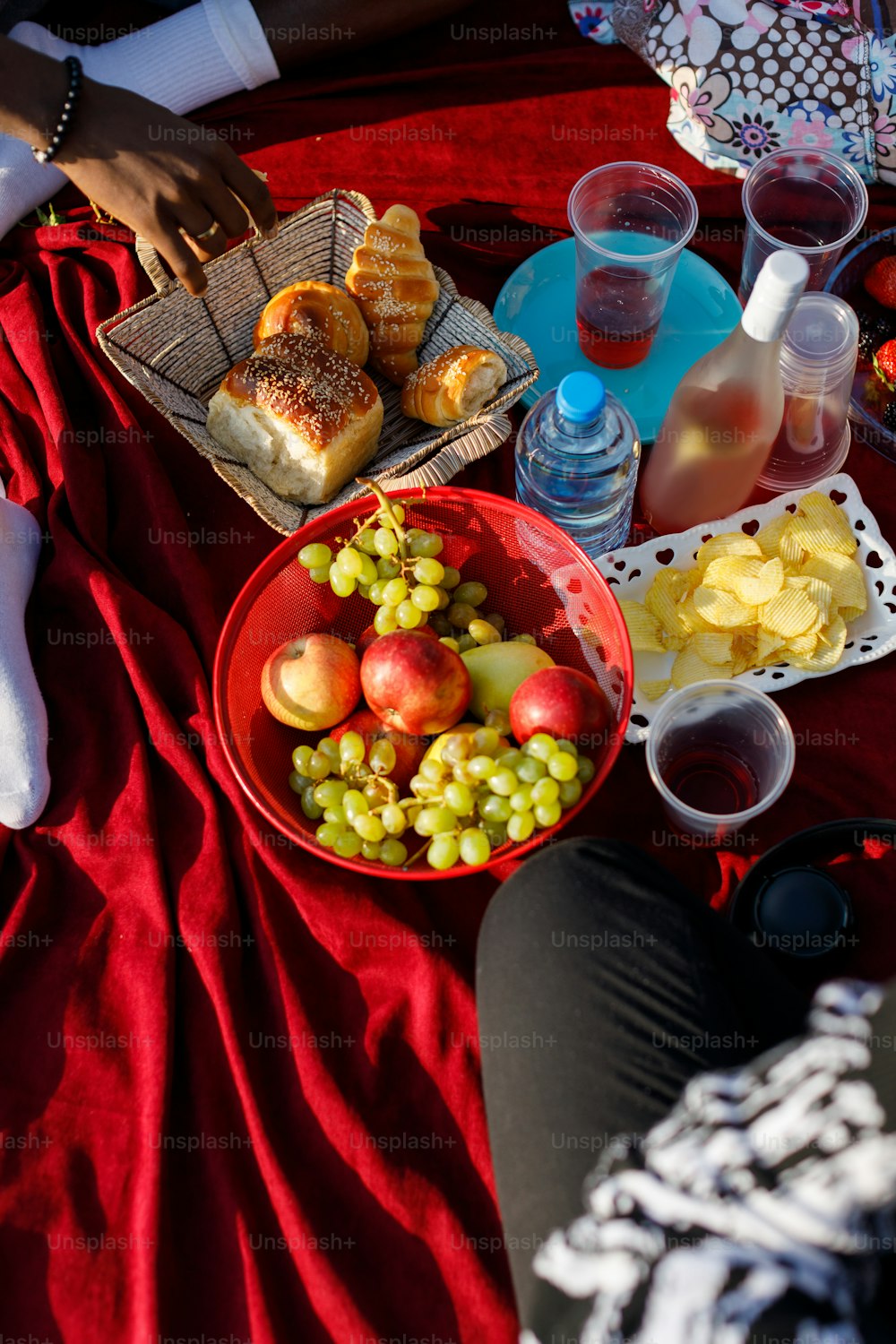 a person sitting on a blanket with a bowl of fruit and a basket of bread