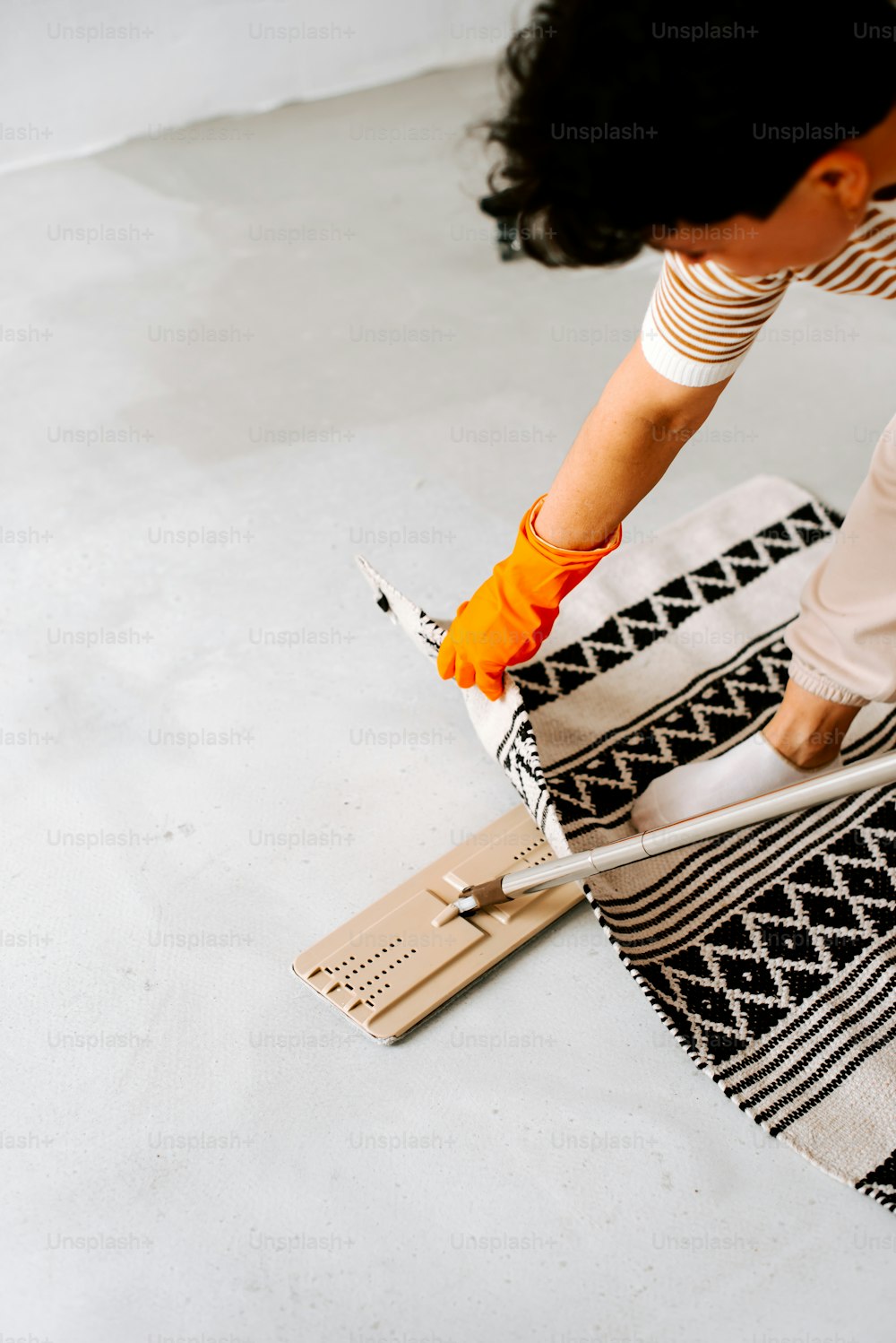 a woman with an orange glove is painting a rug