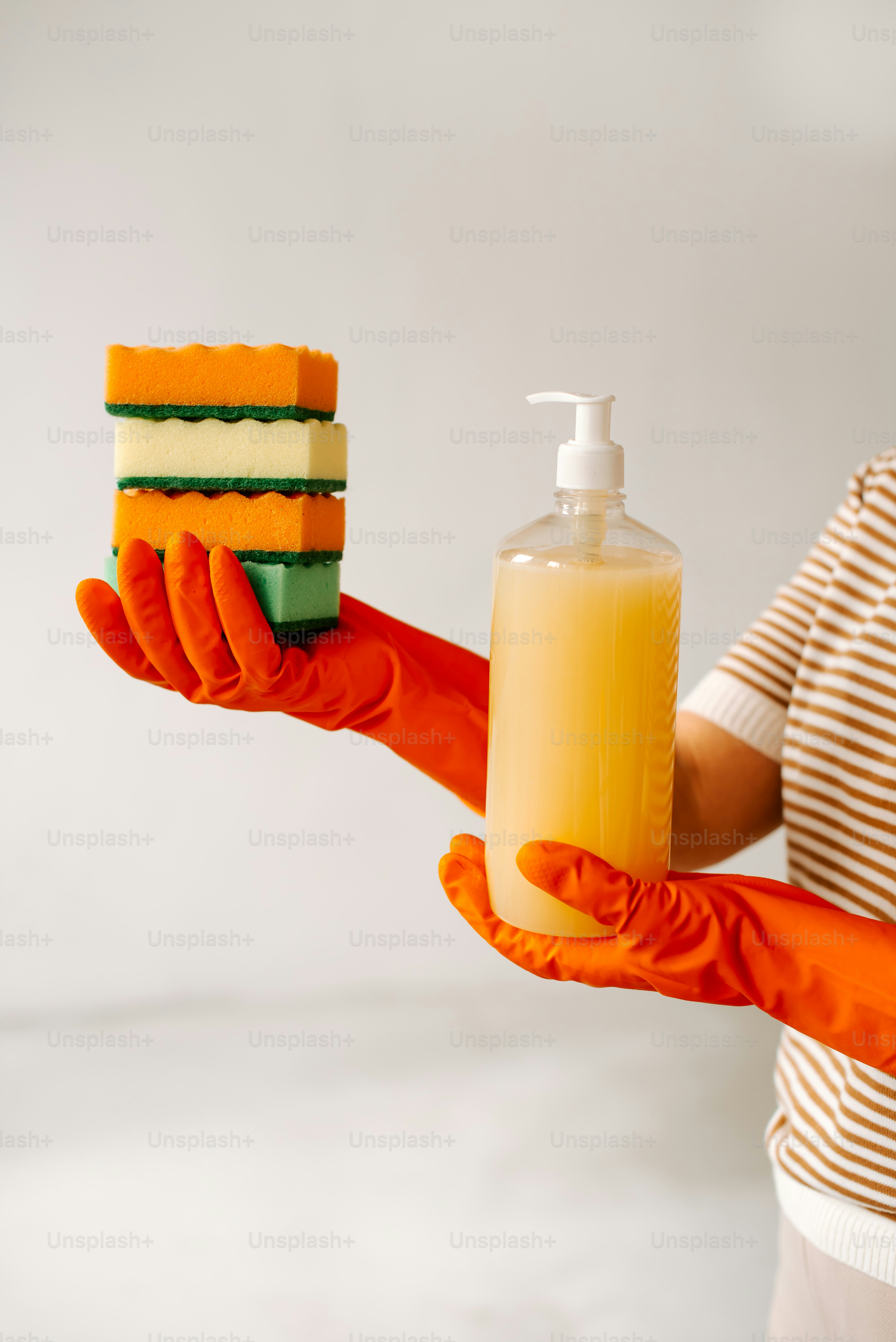 石鹸とスポンジを持つオレンジ色の手袋をはめた人