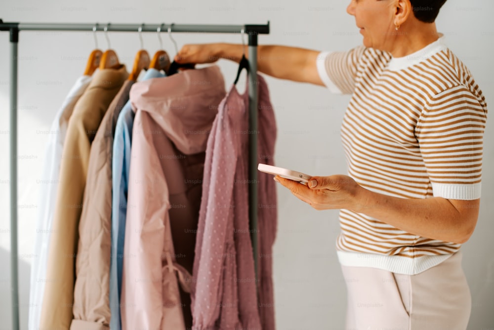 a woman looking at a cell phone in front of a rack of clothes