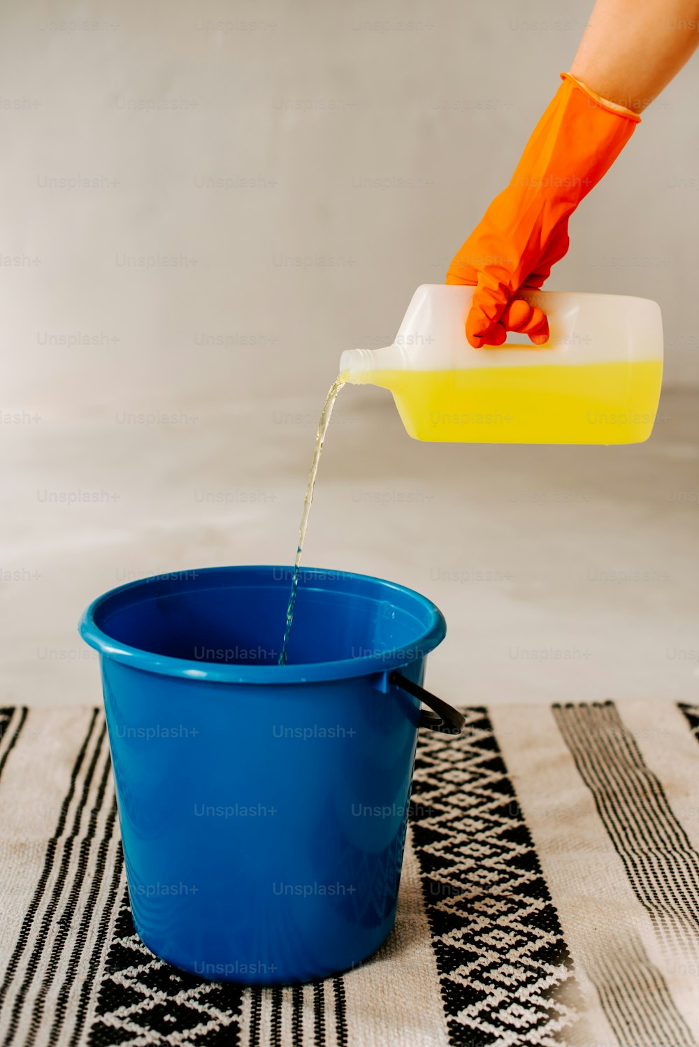 uma pessoa em luvas laranja está derramando água em um balde azul