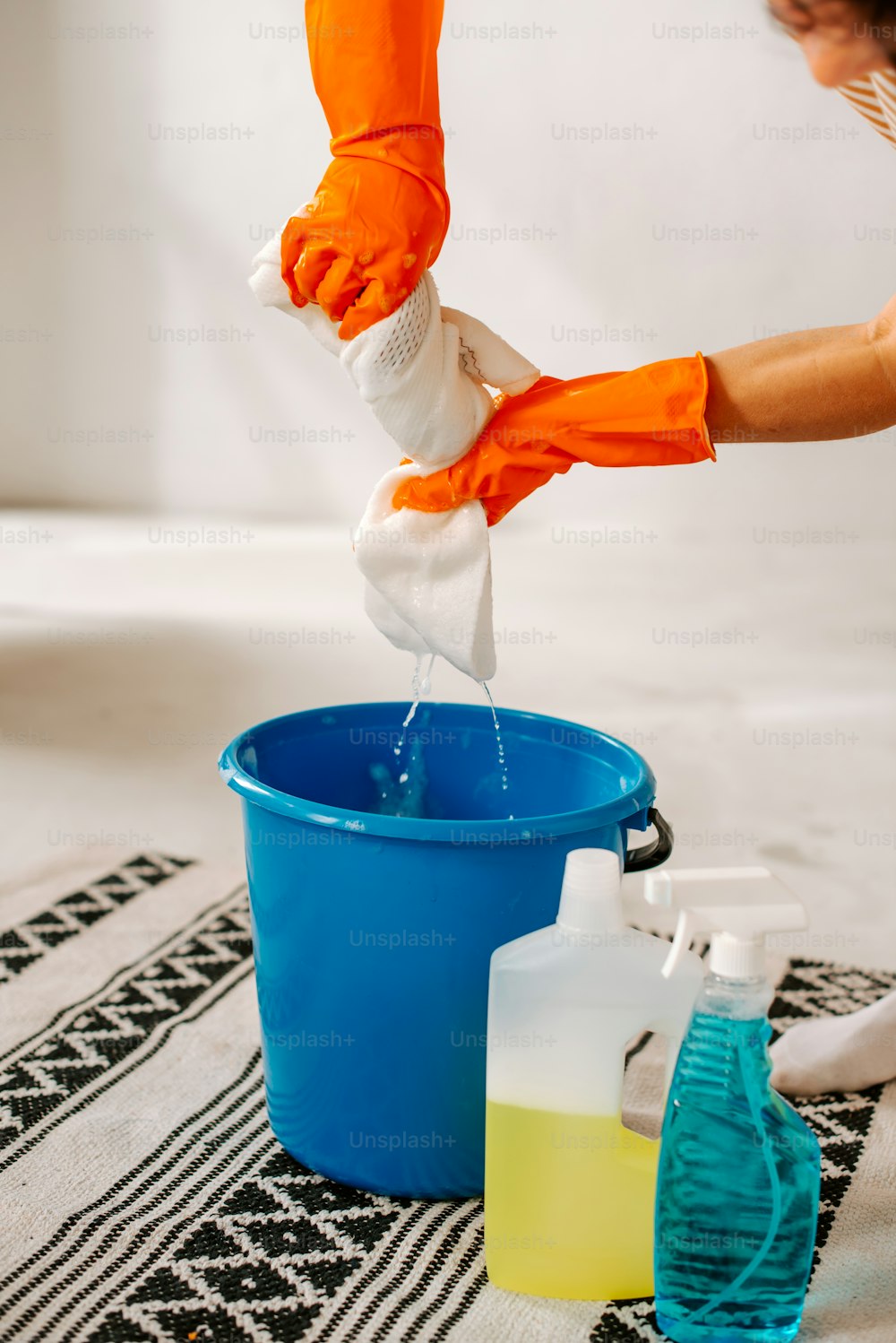 a person in orange gloves is pouring liquid into a blue bucket