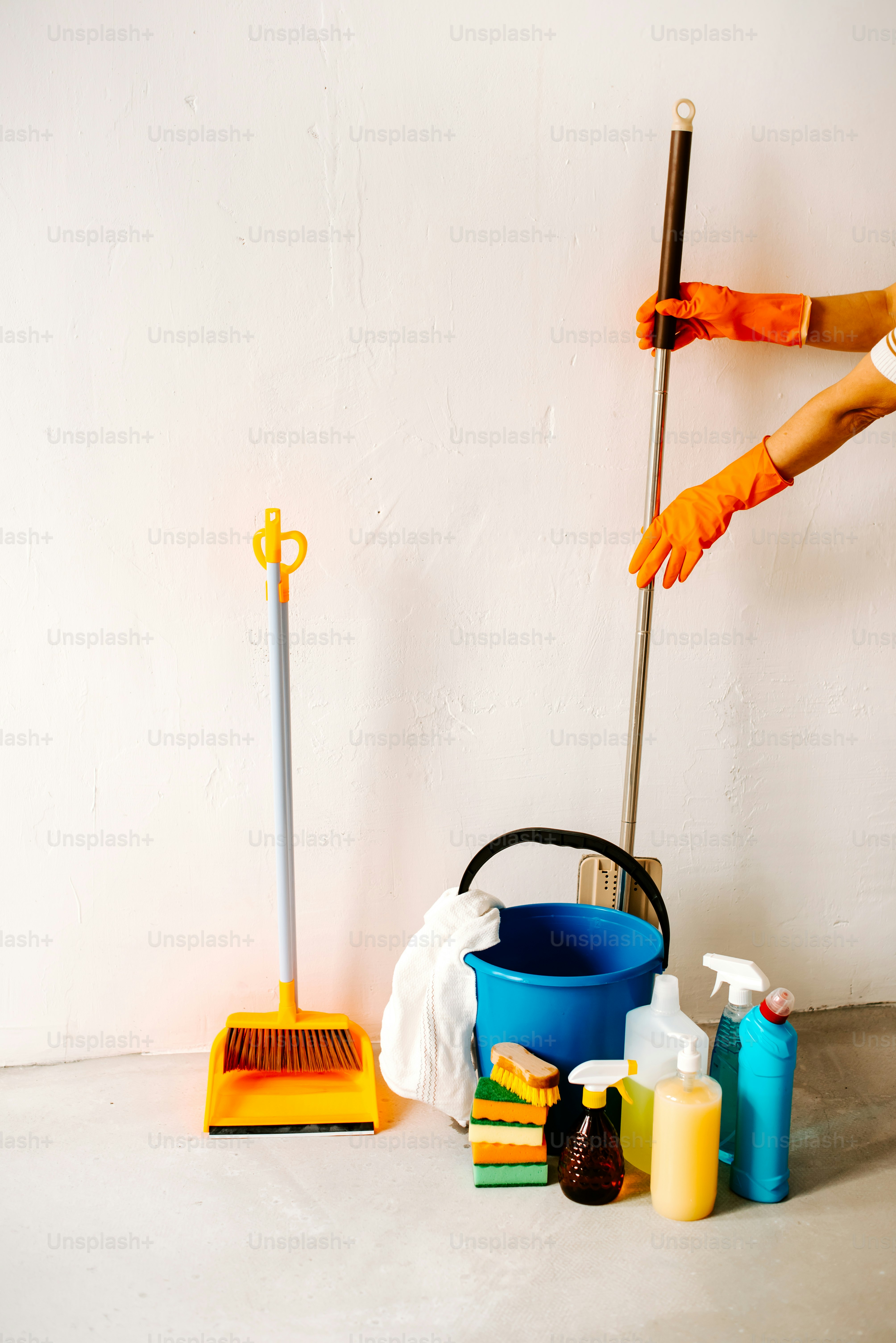 オレンジ色の手袋とゴム手袋をはめた人が床を掃除している