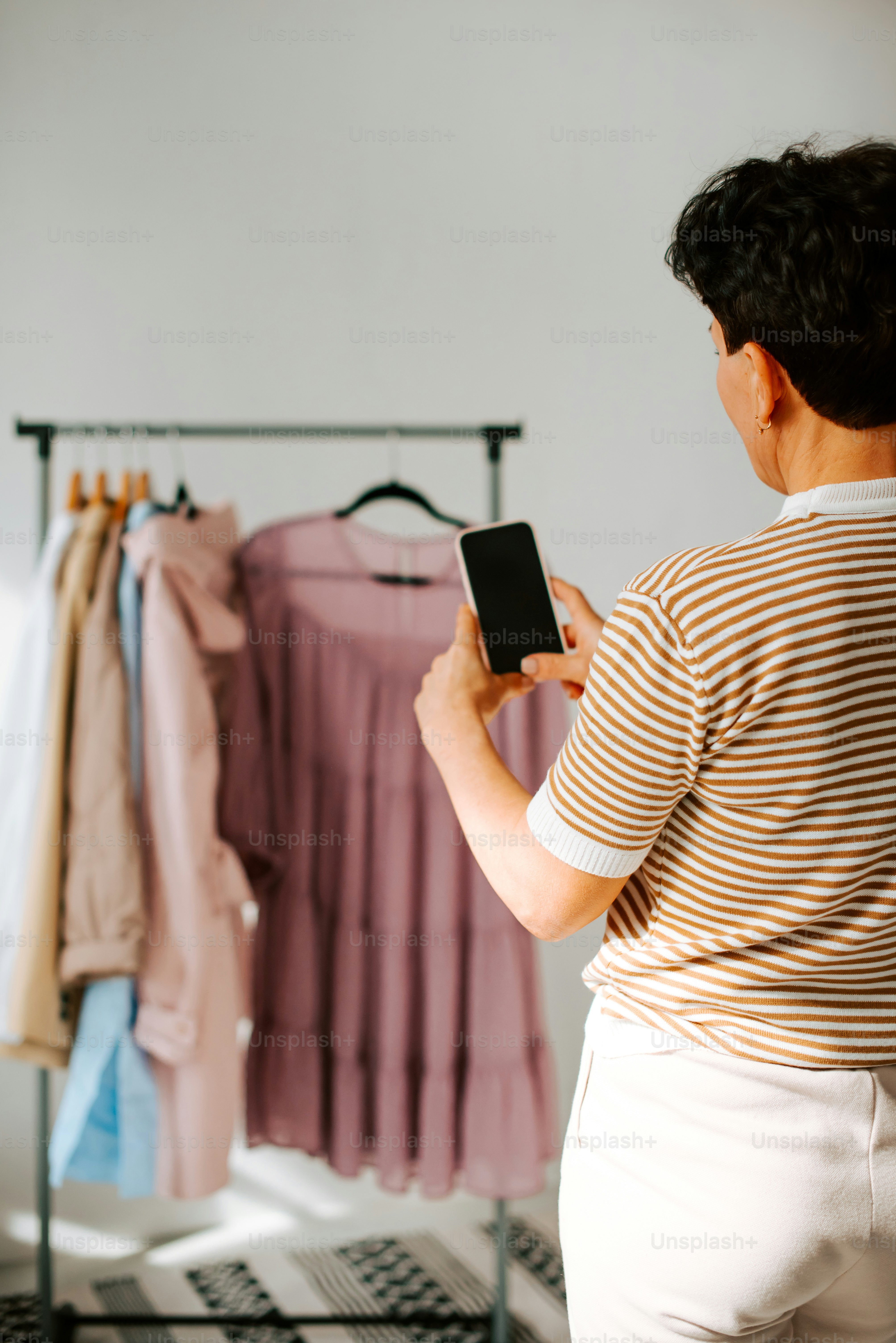 uma mulher em pé na frente de uma prateleira de roupas olhando para um telefone celular