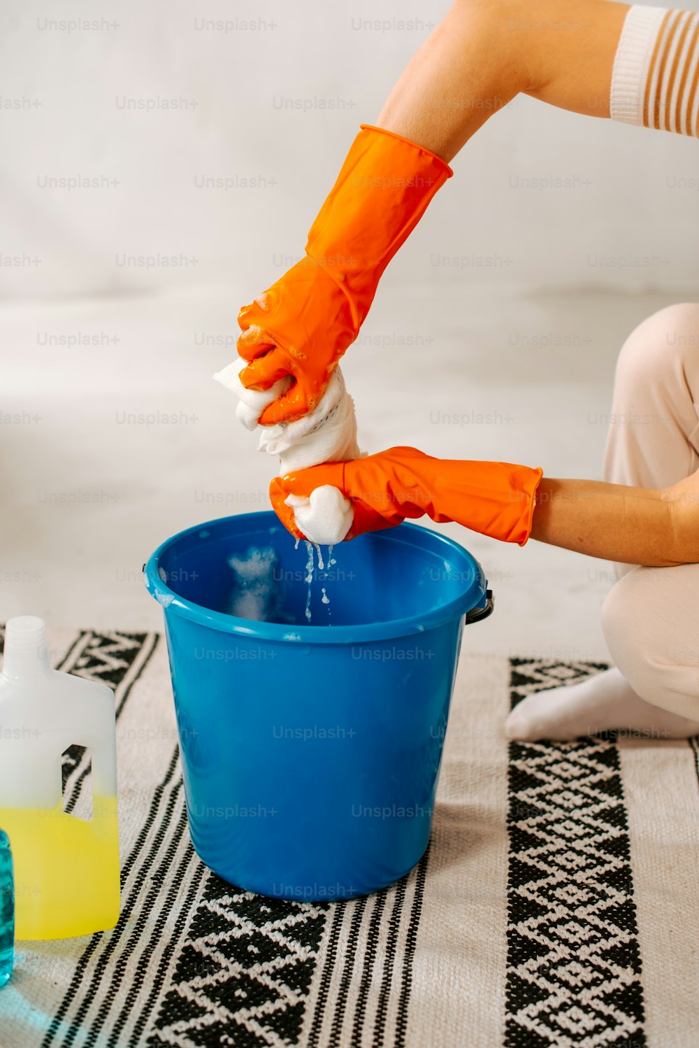 オレンジ色の手袋をはめた人が青いバケツを掃除している
