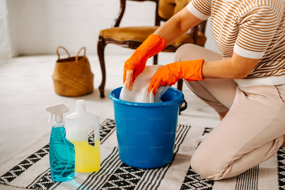Una mujer limpiando un cubo azul con guantes naranjas