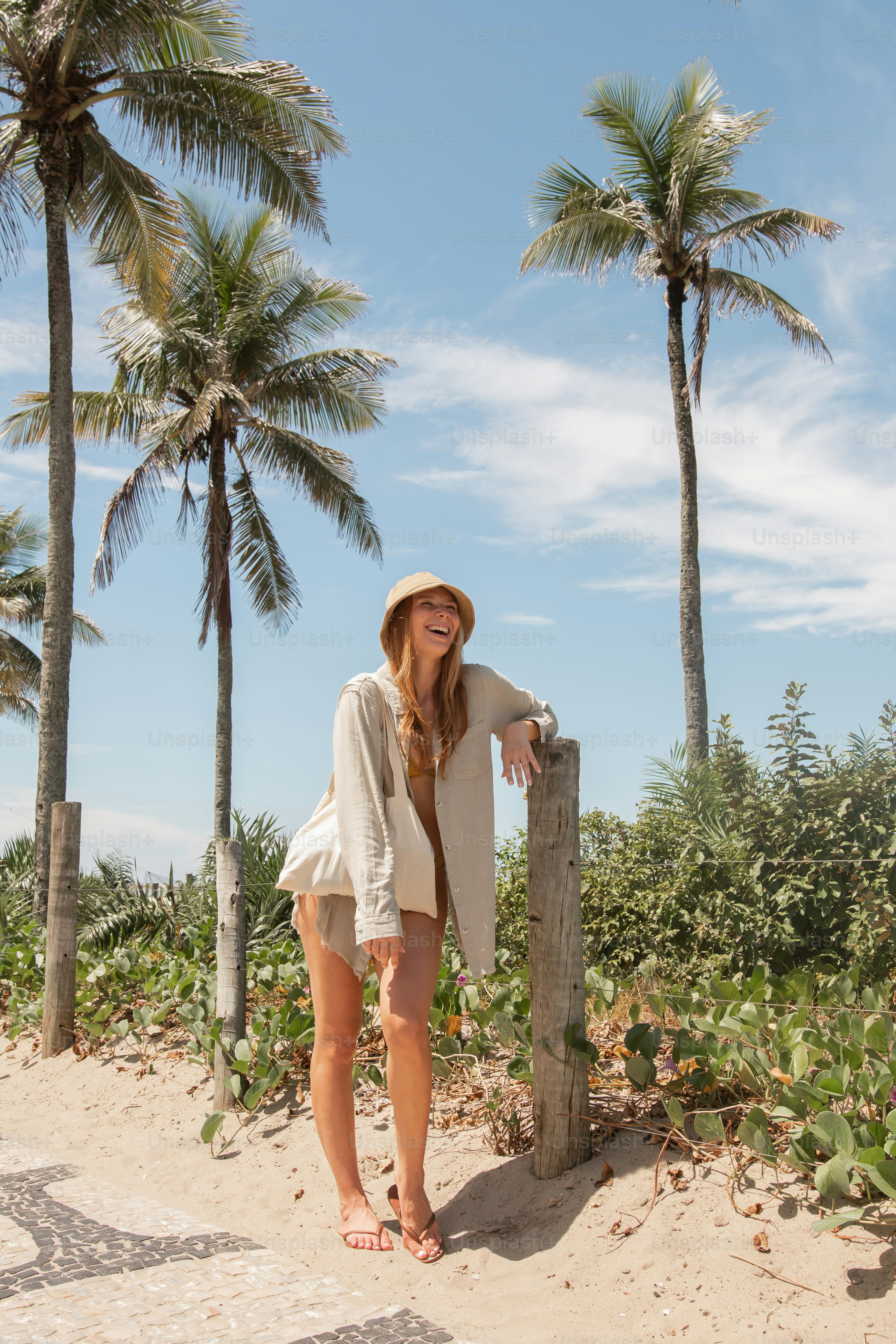 a woman leaning on a wooden post on the beach